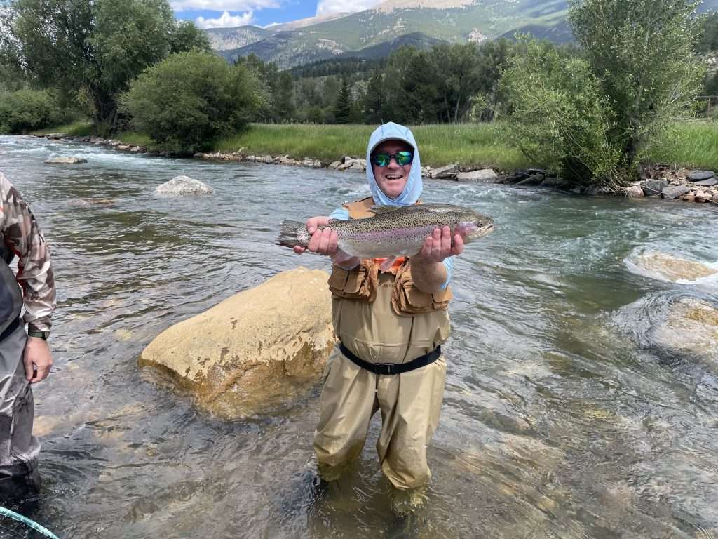 When good fly fishing is bad, man holding a large rainbow fish in a natural river with rocks