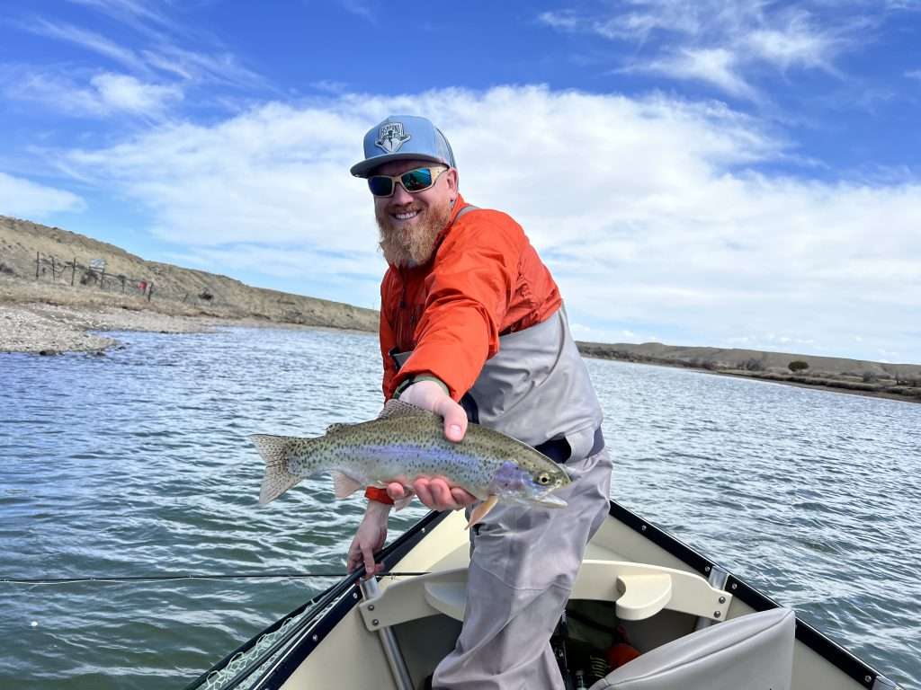 Fishing New Waters - Fly fishing from a drift boat: Part 2, man holding a fish that he caught fly fishing in a drift boat in a natural river